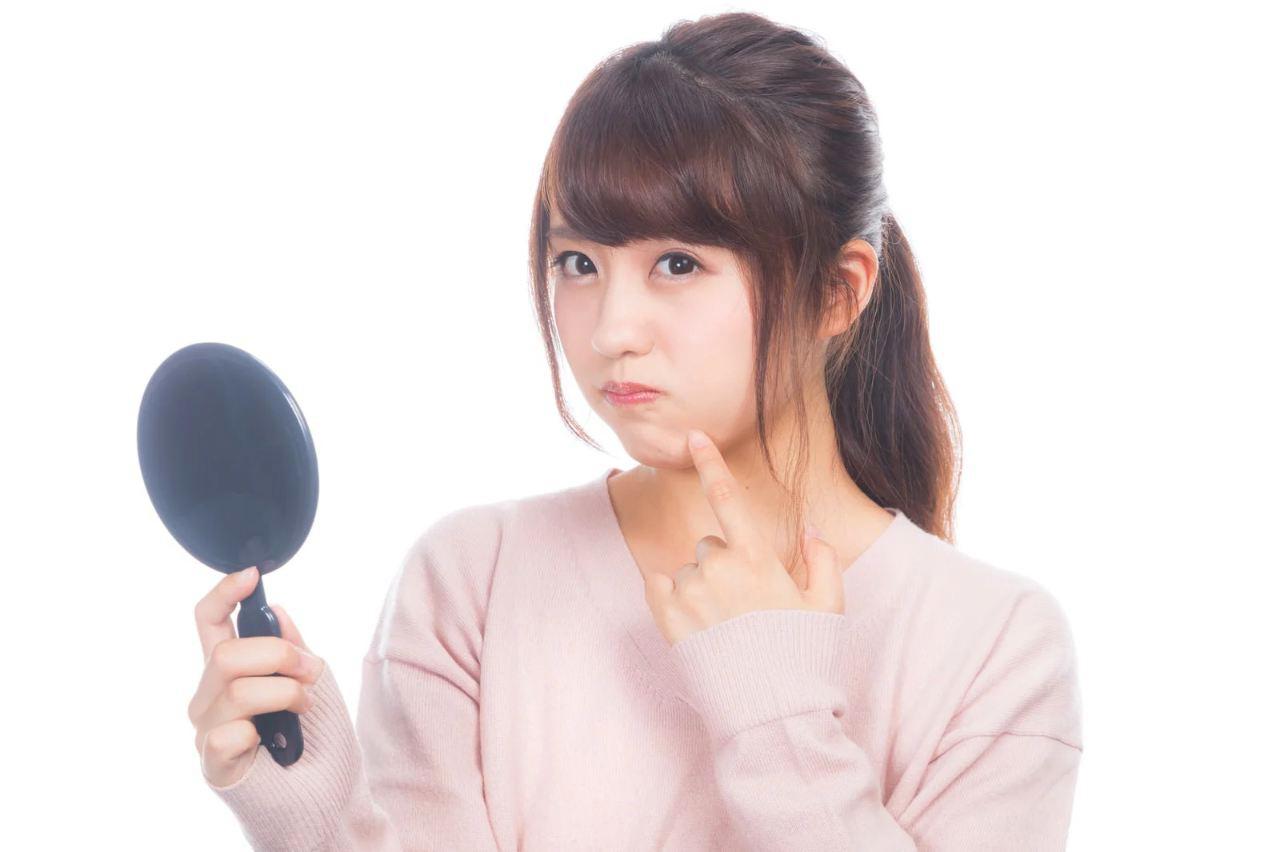 スマホ画面を見つめながら頬やフェイスラインに触れる30代女性のイメージ