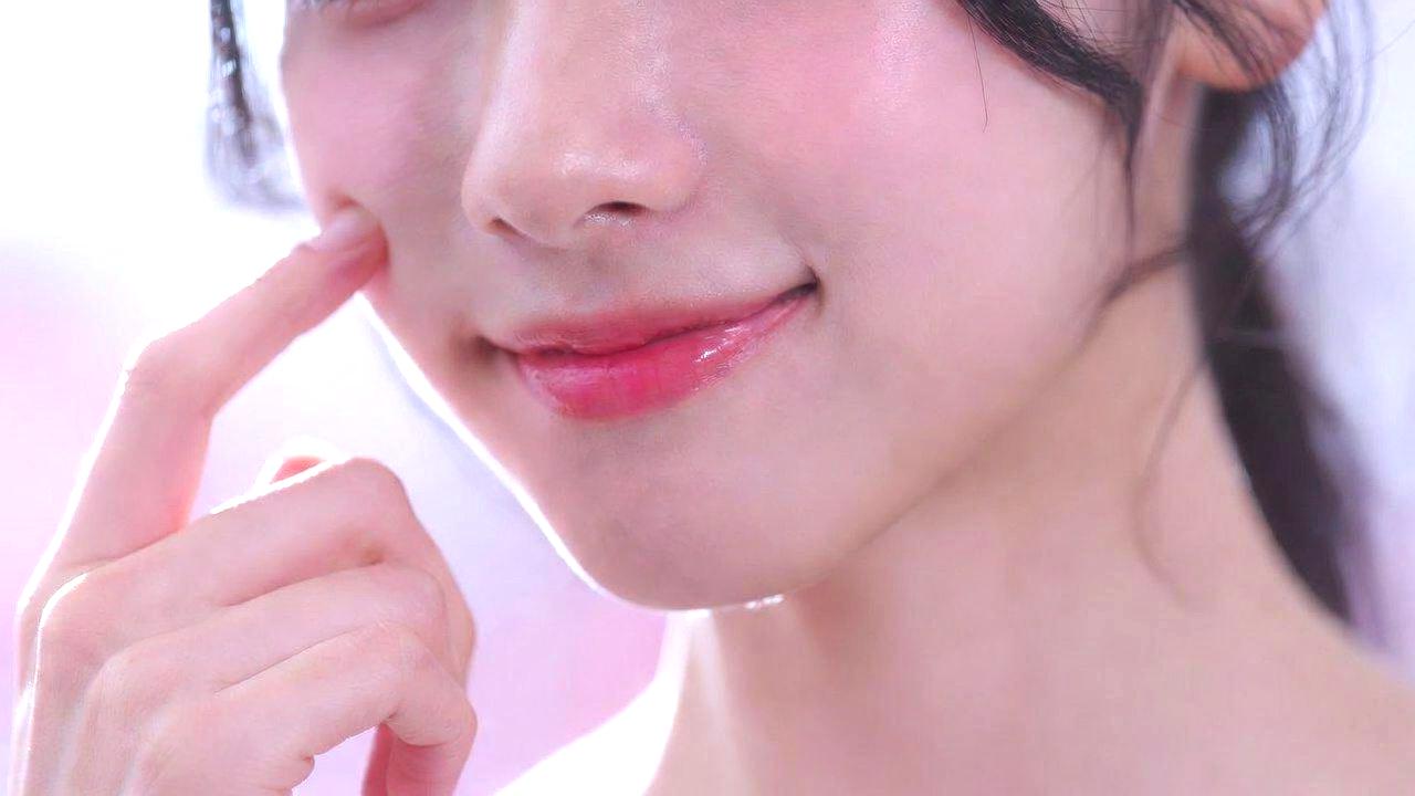 美容液を顔の下から上へ塗り込んでいる女性の手と肌